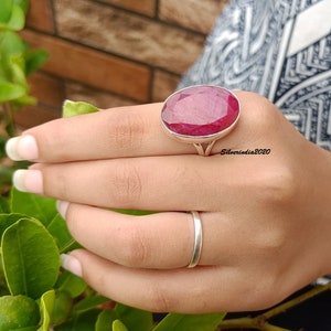 Pode incluir: Um anel de prata com uma grande gema de rubi de corte oval. O rubi &eacute; de cor vermelha profunda e est&aacute; engastado numa moldura de prata simples e elegante. Um anel de banda de prata simples tamb&eacute;m &eacute; vis&iacute;vel. O texto "Silverindia2020" est&aacute; na imagem.