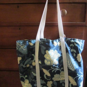 May include: A blue and white floral tote bag with white straps. The bag has a large floral pattern with white flowers and green leaves on a dark blue background.