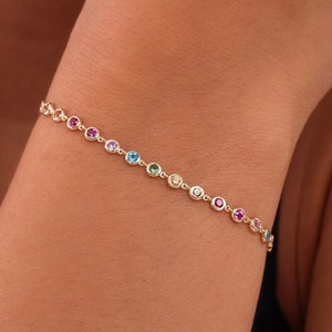 May include: A gold chain bracelet featuring small, colourful gemstones. The gemstones are arranged in a rainbow pattern.