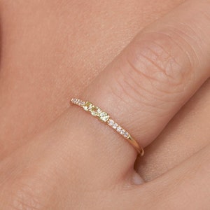 Op de afbeelding: Een delicate gouden ring met een rij kleine, glinsterende diamanten en drie groene edelstenen.