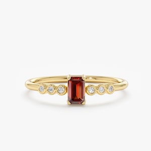 May include: A gold ring with a red gemstone and small diamonds set in the band.