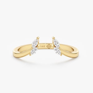 May include: A gold ring with two marquise-shaped diamonds on each side. The ring is open in the center and is designed to be worn as a wedding band enhancer. The ring is marked "14K" on the inside.