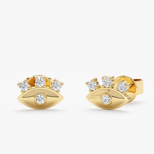 May include: A pair of gold evil eye earrings with small diamonds set in the eye and around the top of the eye.