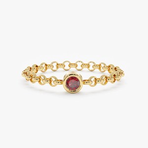 May include: A gold chain ring with a single red gemstone in the center.