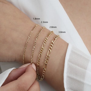 May include: Four gold chain bracelets of different widths, 1.8mm, 2.3mm, 2.8mm, and 3.8mm, are stacked on a person's wrist.