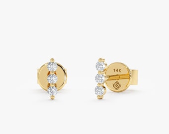 May include: A pair of gold earrings with three small round diamonds set in a vertical line. The earrings are marked "14K" on the back.