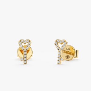 May include: A pair of gold heart key earrings with a diamond-encrusted design. The earrings are 14k gold and feature a heart-shaped key design with a diamond-encrusted outline.