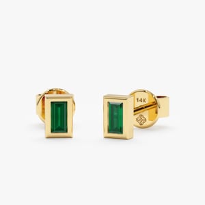May include: A pair of gold earrings with emerald green rectangular gemstones set in a gold frame. The earrings are marked "14K" on the back.