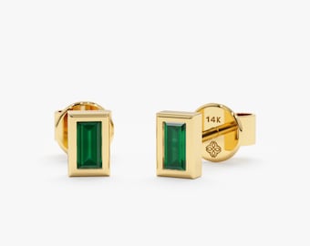 May include: A pair of gold earrings with emerald green rectangular gemstones set in a gold frame. The earrings are marked "14K" on the back.