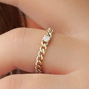 May include: A gold chain ring with a single small diamond in the centre.