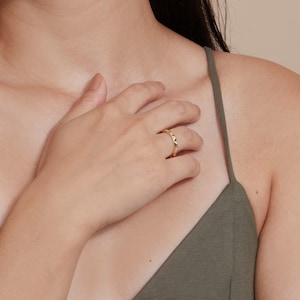 May include: A gold ring with a textured, pointed design. The ring is worn on the finger of a person's hand.