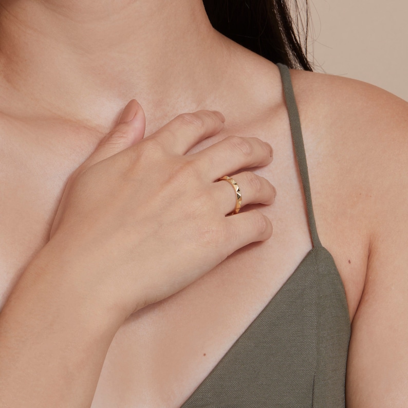 May include: A gold ring with a textured, pointed design. The ring is worn on the finger of a person's hand.