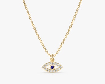 Può includere: Una collana con catena d'oro con un piccolo ciondolo a forma di occhio turco. Il ciondolo è incastonato con piccoli diamanti trasparenti e uno zaffiro blu al centro.