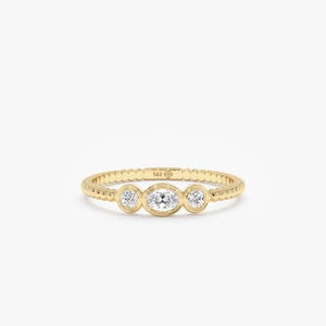 May include: A 14K yellow gold ring featuring a beaded band design. The center of the ring is set with three clear, round and oval-shaped stones in bezel settings. The interior of the band is clearly stamped with the text 14K.