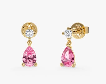 May include: A pair of gold earrings with a pear-shaped pink gemstone hanging from a round, ornate gold setting with a small diamond. The earrings have a post-back closure.