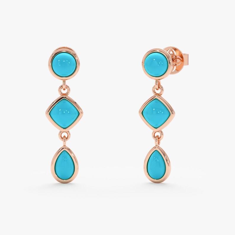 May include: Dangling earrings with a rose gold setting and turquoise blue stones. Each earring features a round stone at the top, a square stone in the middle, and a teardrop-shaped stone at the bottom. The earrings are displayed against a white background.