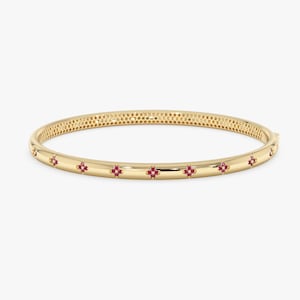May include: A polished gold bangle bracelet featuring a series of evenly spaced, small four-petaled flower motifs. Each flower is set with tiny, vibrant red stones, and the inner surface of the bangle displays a fine, repeating honeycomb pattern.