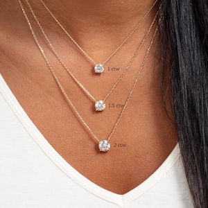 May include: Three gold necklaces, each with a clear, round gemstone. The necklaces are labelled with the text: 1 ctw, 1.5 ctw, and 2 ctw. The necklaces are displayed on a person wearing a white top.