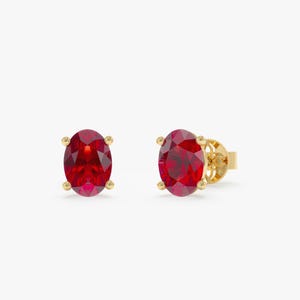 May include: A pair of gold stud earrings with oval-shaped red ruby gemstones.