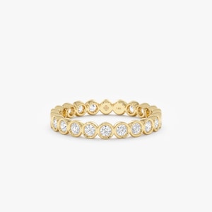 May include: A gold-colored ring with a continuous row of clear, round gemstones. The ring has a polished finish and a simple, elegant design, suitable for everyday wear or special occasions. The gemstones are evenly spaced around the band.