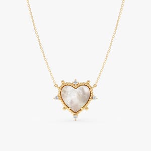 May include: A gold-colored necklace featuring a heart-shaped pendant. The pendant has a pearlescent center, surrounded by a gold frame with small, clear gemstones. The necklace chain is delicate and gold.