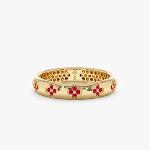 May include: A 14K yellow gold band ring featuring a repeating pattern of four-petaled flower motifs, each set with four small round red rubies. The interior of the band has a honeycomb-textured surface and is stamped with the text 14K.