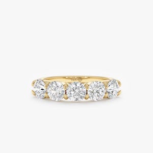 May include: A gold ring with five clear, round diamonds set in a row. The diamonds are closely spaced, creating a continuous sparkle. The ring is set against a white background, highlighting the gemstones' brilliance.
