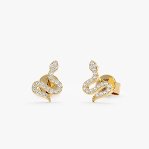 Pode incluir: Um par de brincos de cobra de ouro com detalhes de diamantes. Os brincos são feitos de ouro 14 quilates e apresentam um design delicado de cobra com diamantes brilhantes.