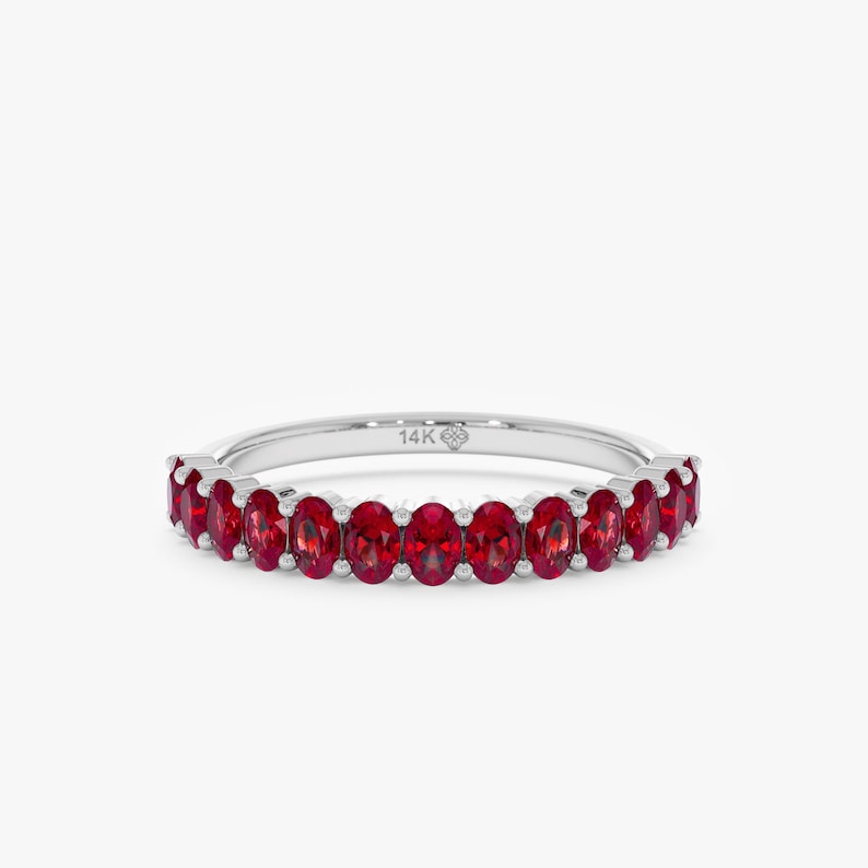 K&ouml;nnte beinhalten: Ein silberner Ring mit einer Reihe oval geschliffener, leuchtend roter Edelsteine. Der Ring ist mit "14K" markiert und hat ein filigranes Design, das die Farbe und den Glanz der Edelsteine hervorhebt. Ein klassisches Schmuckst&uuml;ck.