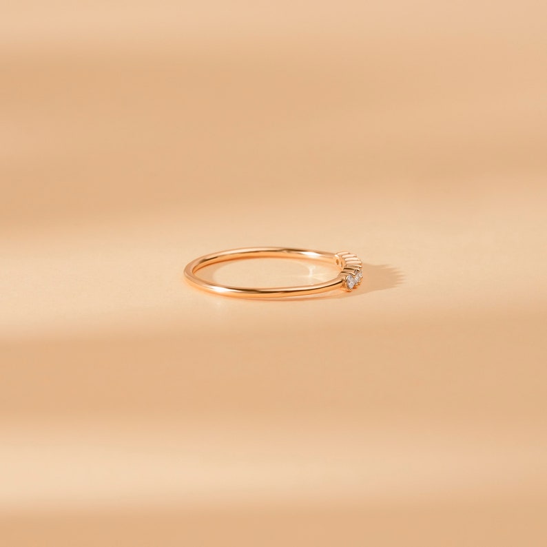 May include: A delicate gold band ring with a row of small diamonds set in a curved line.