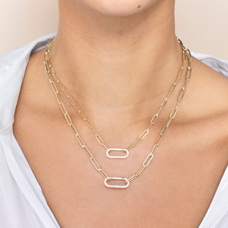 May include: A gold chain necklace with two oval-shaped pendants. Each pendant is set with small, clear stones.