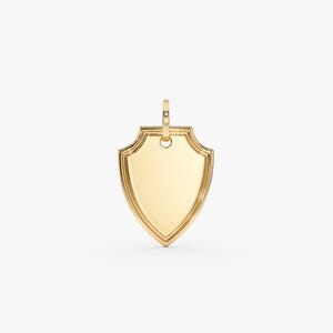 Pode incluir: Pingente dourado em forma de escudo com acabamento polido. O pingente tem formato de escudo clássico com borda decorativa e uma pequena argola na parte superior para uma corrente. O pingente tem aproximadamente 3,8 cm de altura.