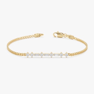 Op de afbeelding: Een delicate gouden armband met een kettingontwerp en een reeks kleine, sprankelende diamanten. De armband heeft een veilige sluiting en is ontworpen voor dagelijks gebruik. De diamanten zijn lineair gerangschikt.