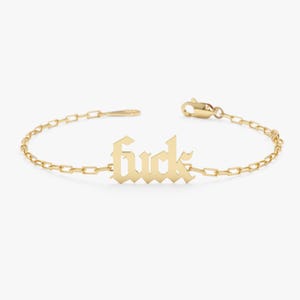May include: Gold-toned bracelet featuring the word "fuck" in a gothic font. The bracelet has a delicate chain design with a lobster clasp closure. The word is centered on the chain.