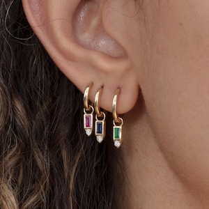 May include: Three gold hoop earrings with dangling charms. Each charm features a small rectangular gemstone in red, blue, and green, with a tiny diamond accent.