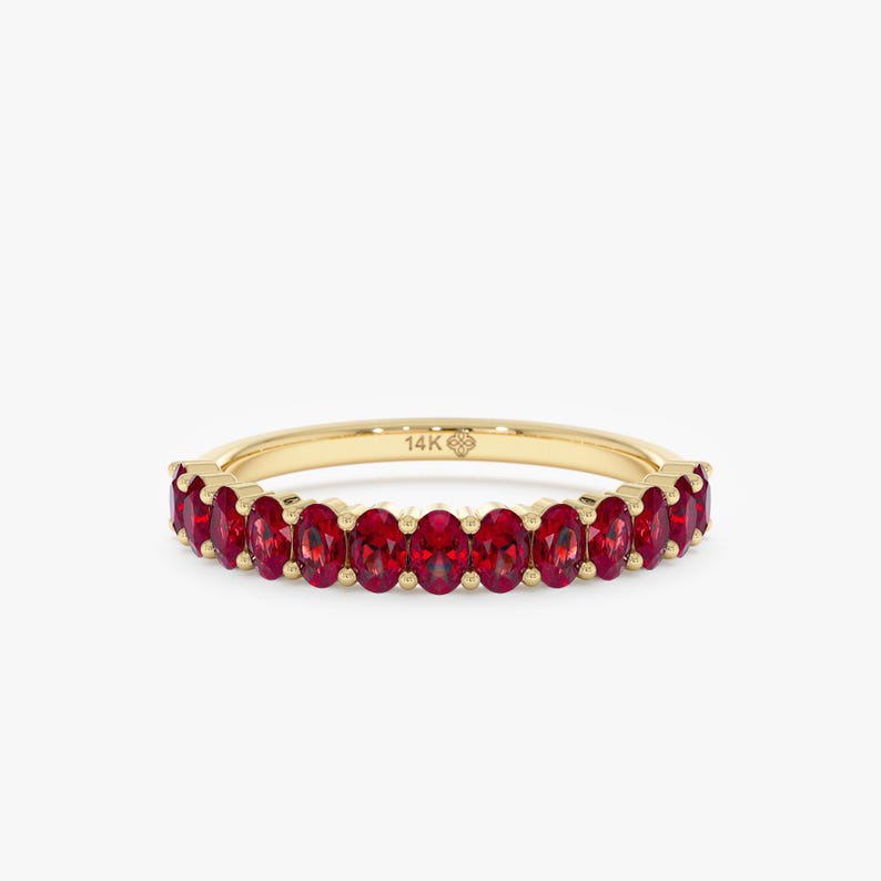 K&ouml;nnte beinhalten: Ein goldener Ring mit oval geschliffenen roten Edelsteinen. Der Ring ist aus d&uuml;nnem, poliertem Gold. Die Edelsteine sind gleichm&auml;&szlig;ig angeordnet. Der Ring ist mit "14K" gekennzeichnet.