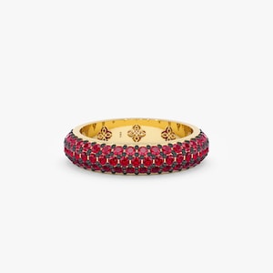 Op de afbeelding: Een gouden ring met drie rijen rode edelstenen. De ring is bezet met kleine, ronde stenen.