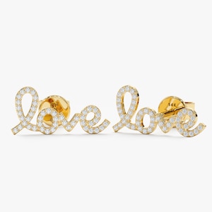 Könnte beinhalten: Ein Paar goldene Ohrstecker mit dem Wort "love" in Schreibschrift. Die Buchstaben sind mit kleinen, funkelnden weißen Edelsteinen besetzt. Die Ohrringe haben einen Stecker und einen Verschluss für sicheren Halt.