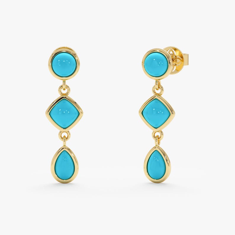 May include: A pair of gold-colored drop earrings with turquoise-colored stones. Each earring features a round stone at the top, a square stone in the middle, and a teardrop-shaped stone at the bottom. The earrings are displayed against a white background.