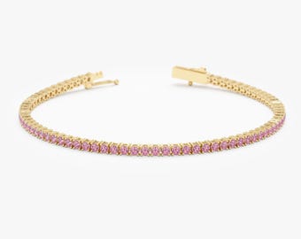 May include: A gold tennis bracelet with pink gemstones. The bracelet is made of a delicate chain with small, round stones set in a continuous line.