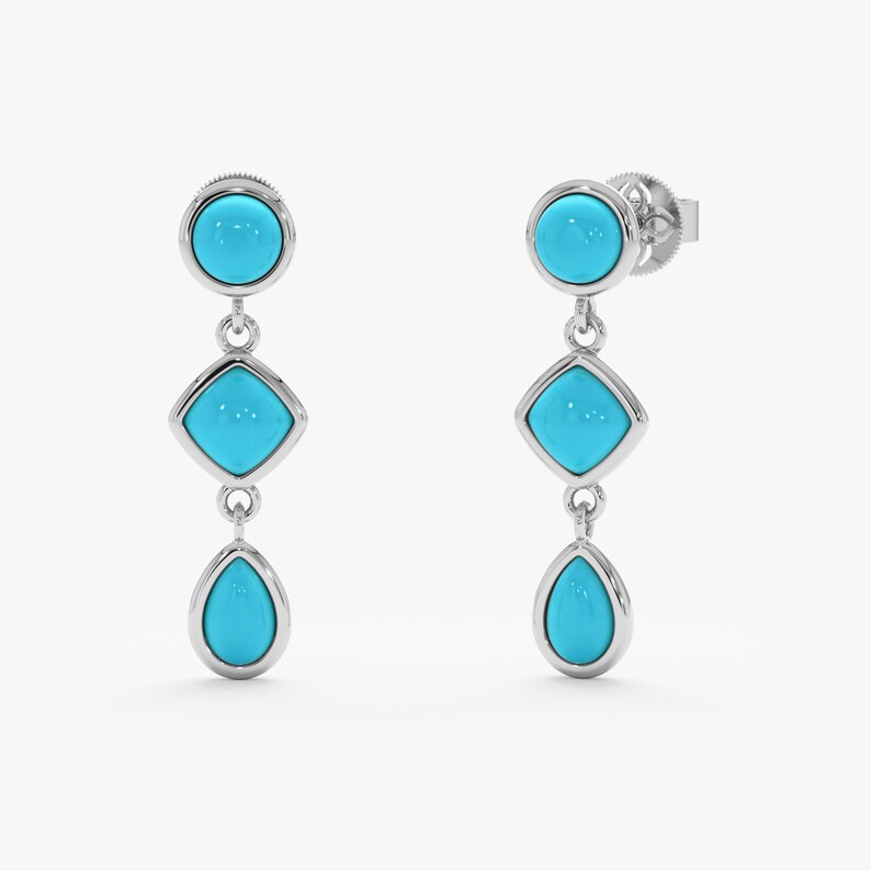 May include: A pair of silver drop earrings with turquoise-colored stones. Each earring features a round stone at the top, a square stone in the middle, and a teardrop-shaped stone at the bottom. The stones are set in a silver bezel.
