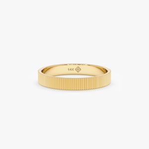 May include: A gold ring with a ribbed texture. The ring is a band style, with a flat surface and vertical grooves. The inside of the ring is stamped with "14K" and a small floral design. The ring is set against a white background.