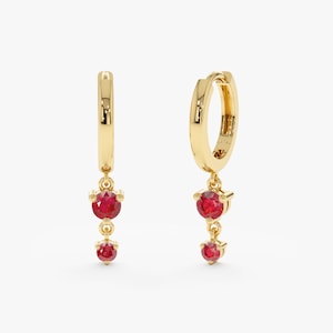 May include: Gold hoop earrings with a dangling chain and two red gemstones.