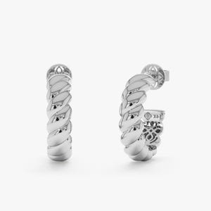 May include: A pair of silver-colored hoop earrings with a twisted rope design. The earrings have a post closure and are displayed against a white background. The earrings are a jewelry item.
