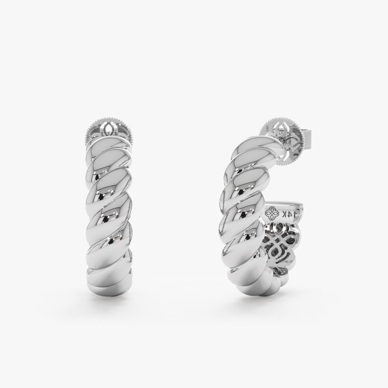 May include: A pair of silver-colored hoop earrings with a twisted rope design. The earrings have a post closure and are displayed against a white background. The earrings are a jewelry item.