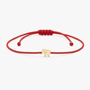 May include: A red string bracelet featuring a small gold elephant charm with a single diamond accent. The bracelet has an adjustable sliding knot closure.