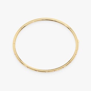 May include: A circular gold bangle bracelet featuring a polished metallic finish and a series of small, evenly spaced red gemstones embedded along the outer edge. The bracelet includes a visible hinged clasp mechanism on the side for opening.