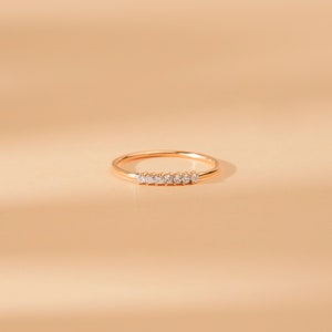 May include: A delicate gold band ring with a row of small, clear diamonds set in the center.