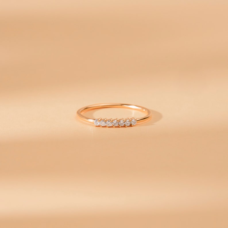 May include: A delicate gold band ring with a row of small, clear diamonds set in the center.