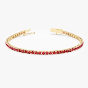 May include: A gold tennis bracelet with a row of red gemstones.